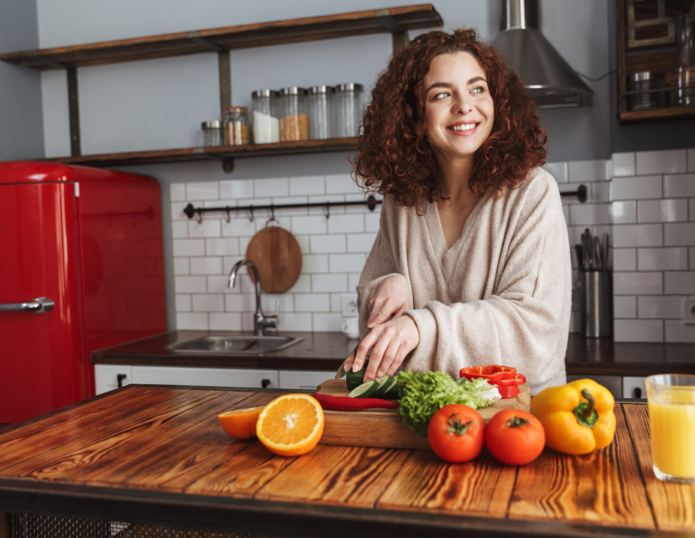 woman smiling while cooking salad with fresh vegetables in kitchen interior at home
