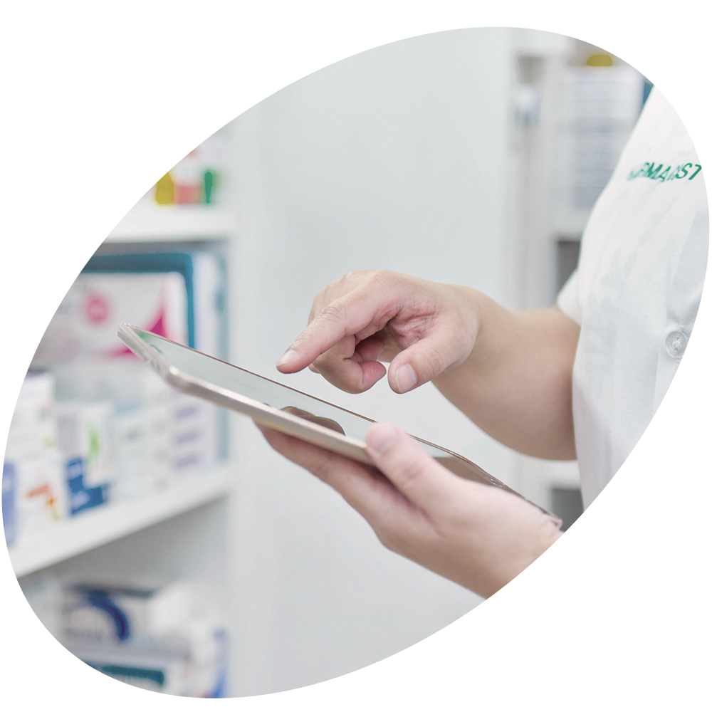 Pharmacist's hands working on tablet with medication in background.